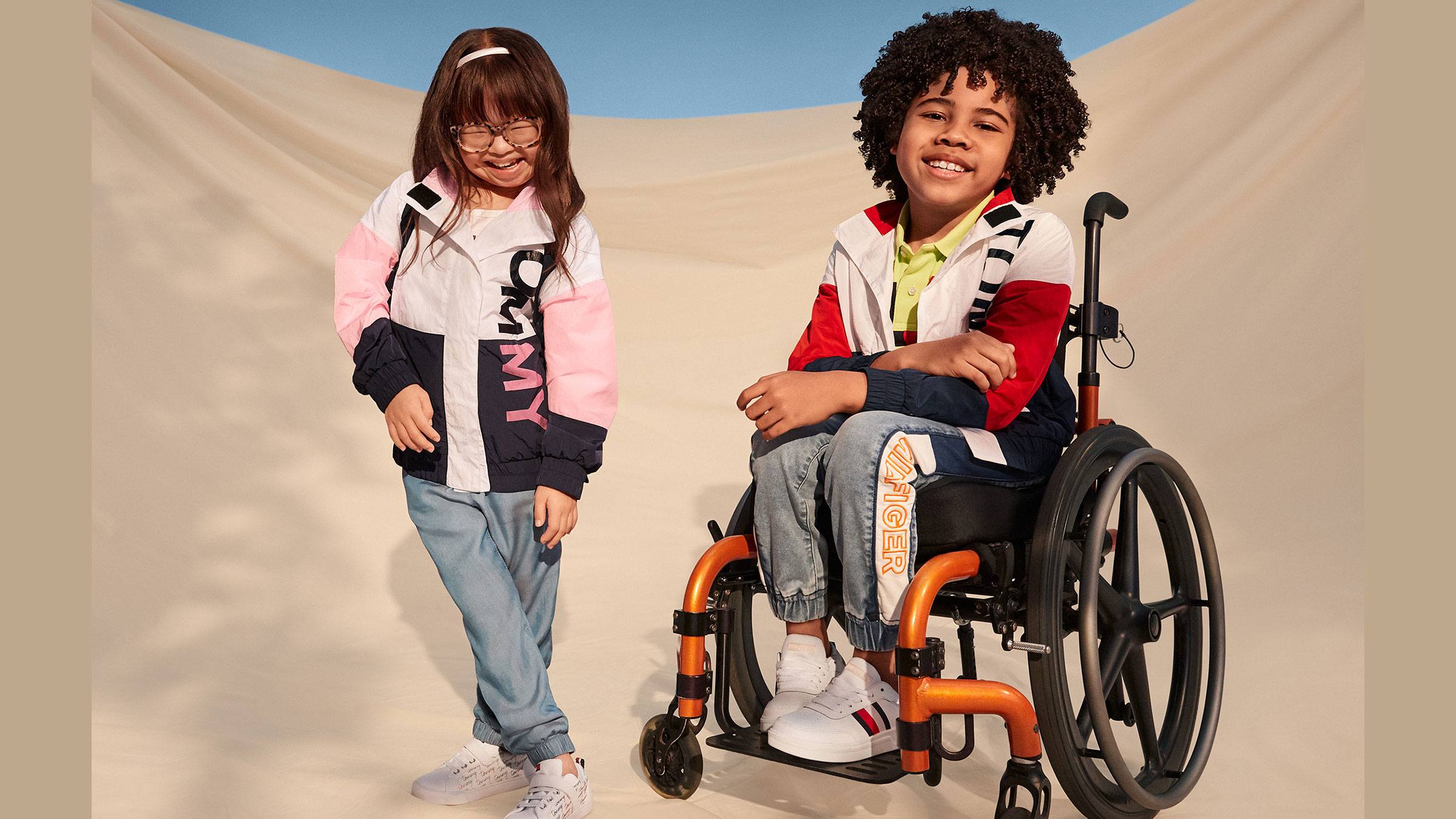 Two visibly disabled children, one boy and one girl, sit in front of a white backdrop wearing Tommy Hilfiger's adaptivewear line. 