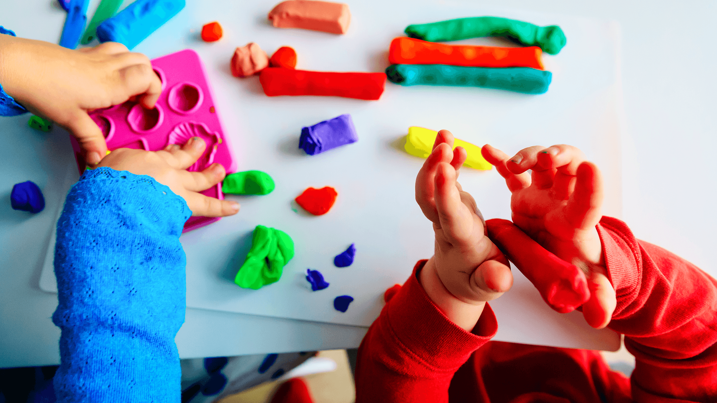 A photo of two children's hands playing with play-dough on a nursery table