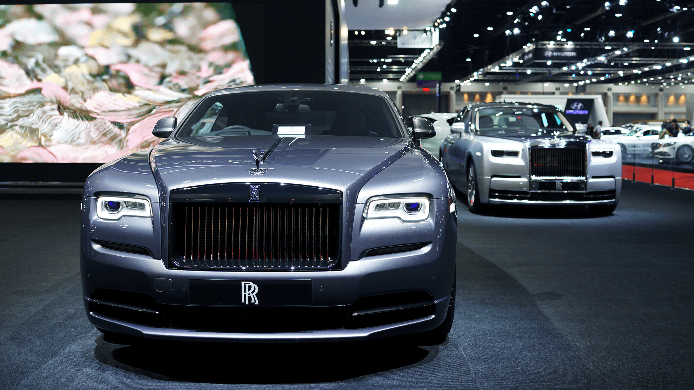 Two silver Rolls Royce cars sit side by side at an expo